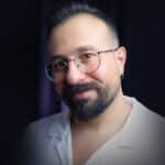 Gözlüklü ve sakallı, beyaz gömlek giymiş Hasan Tuzcu'nun portresi.
