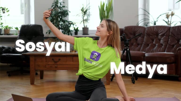 Yeşil Hatu Digital tişörtü giyen bir kadın, yoga yaparken selfie çekiyor, arka planda tripodlu bir kamera var