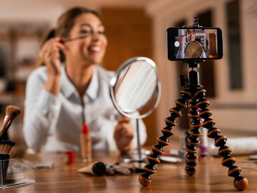 Makyaj yaparken sosyal medyada özgün içerik üreten bir kadın; video kaydı için tripod ve telefon kullanıyor.